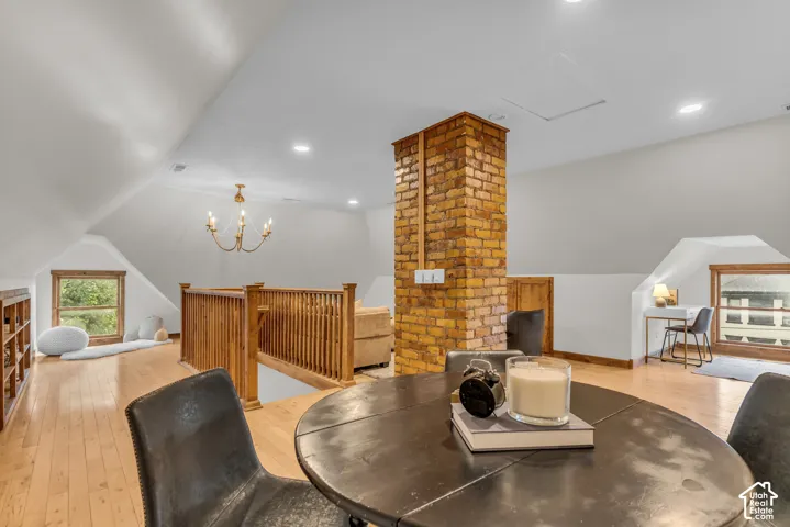 Vaulted ceiling featuring an exposed brick pillar, wood-finish flooring, wood railing, and recessed lighting
