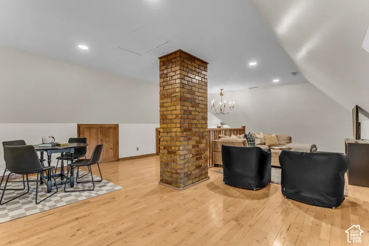 Open-concept space featuring wood-finish flooring, a central exposed brick pillar, recessed ceiling lighting, sloped ceilings, and a wooden balustrade