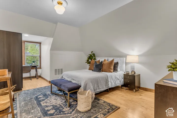 Sloped ceiling architecture featuring wood-finish flooring, a flush-mount overhead light fixture, and an integrated closet with dark-finish doors