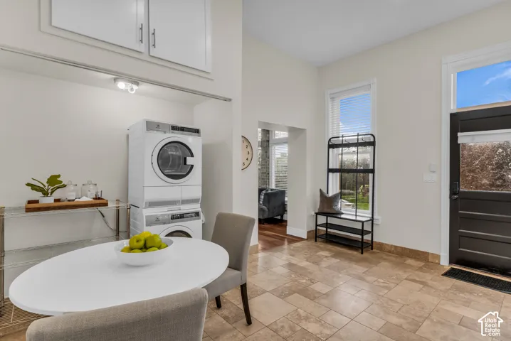 Natural stone tile flooring, stacked laundry appliances, built-in upper cabinetry, and a door featuring an inset glass panel