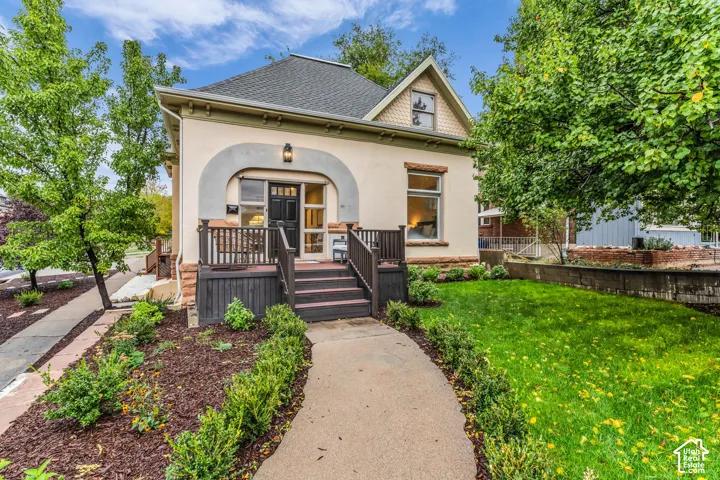 Stucco exterior featuring decorative arched trim, a raised wooden front porch, stone foundation accents, and textured gable siding