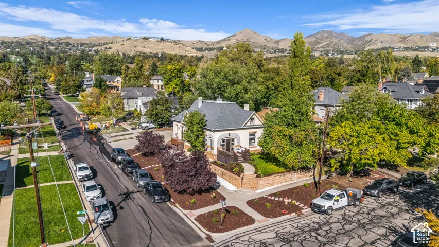 Corner-lot residence featuring a light-toned stucco exterior, asphalt shingle roof, dark wood-finish front porch, and brick masonry perimeter wall with mature landscaping