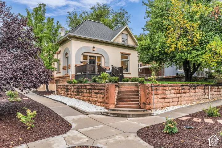 Exterior featuring a stucco facade, arched entryway, dark wood-finish porch railing, and a stone retaining wall with matching stone staircase