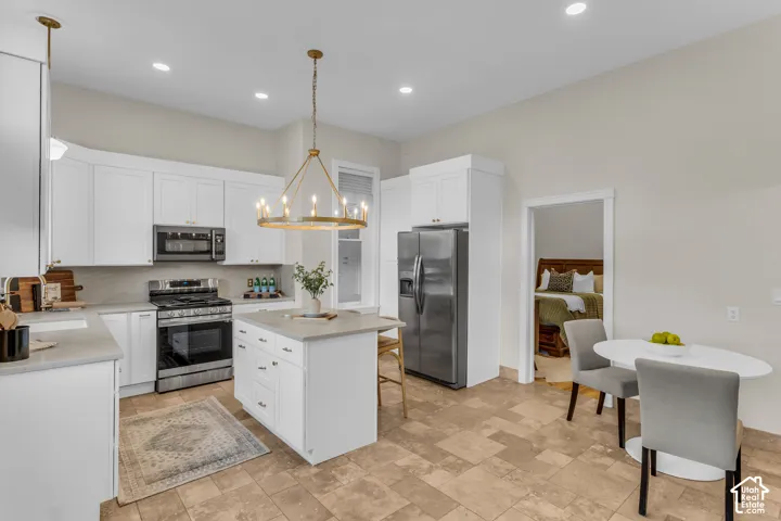 Kitchen featuring white shaker-style cabinetry, a central island with a solid surface countertop, stainless steel appliances, a metallic chandelier, and tile flooring