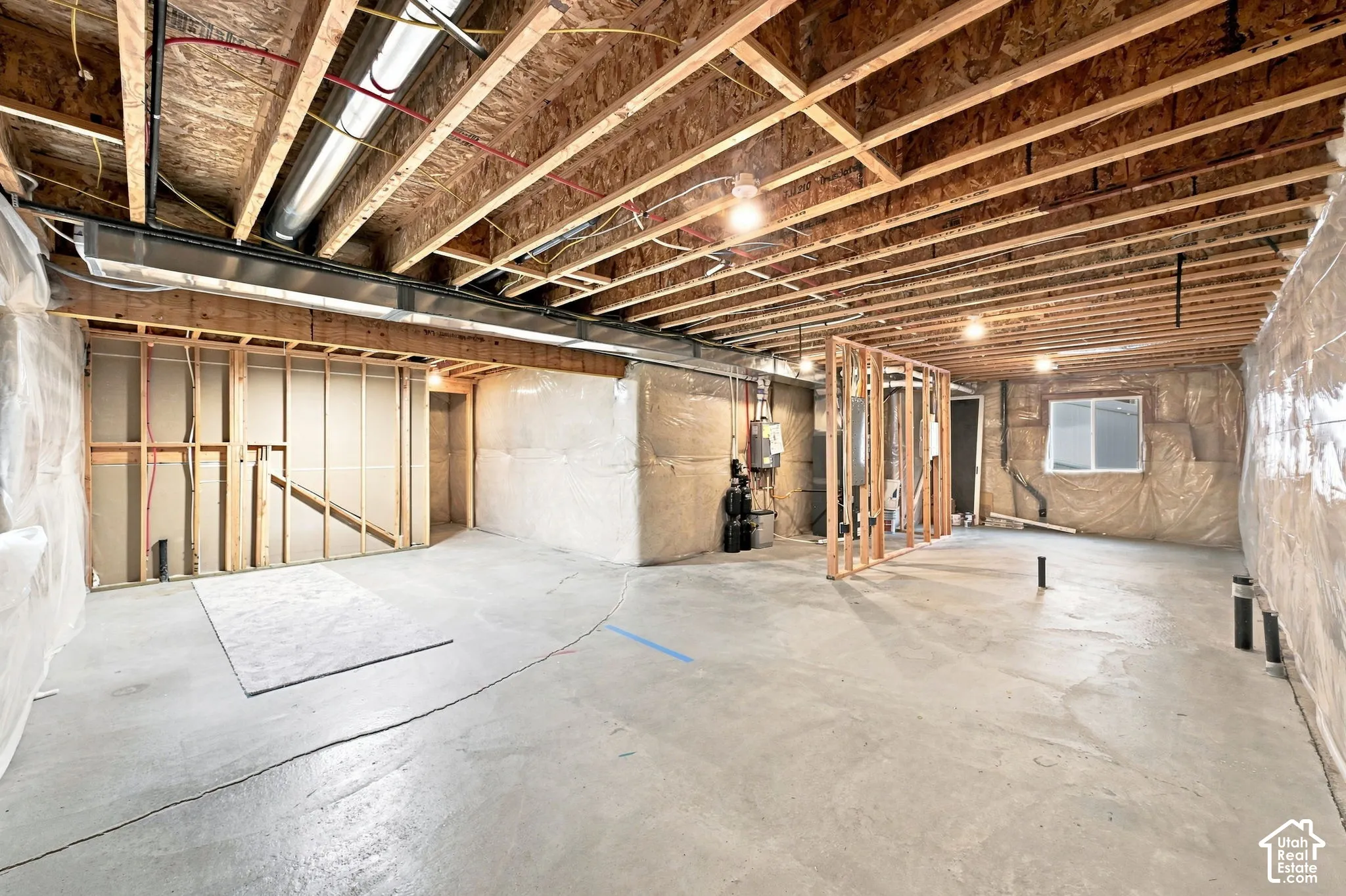 Unfinished lower level featuring exposed wood joist ceilings, concrete flooring, insulated wall segments, and a single window