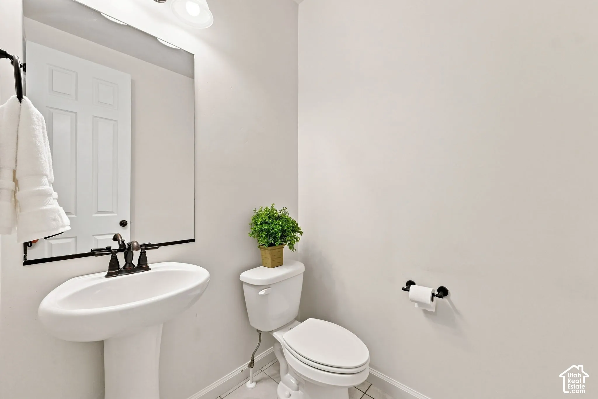 White pedestal sink with a dark metal widespread faucet, large rectangular mirror, and dark metal hardware fixtures