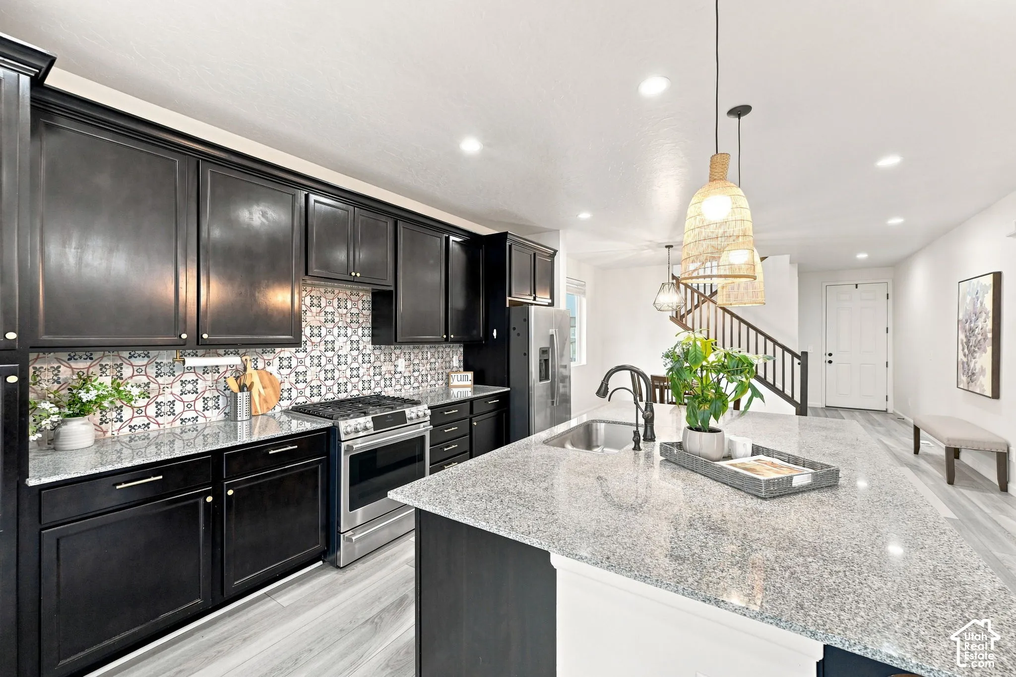 Kitchen featuring dark cabinetry, stone-surface countertops, decorative tile backsplash, stainless steel gas range, and a center island with an undermount sink