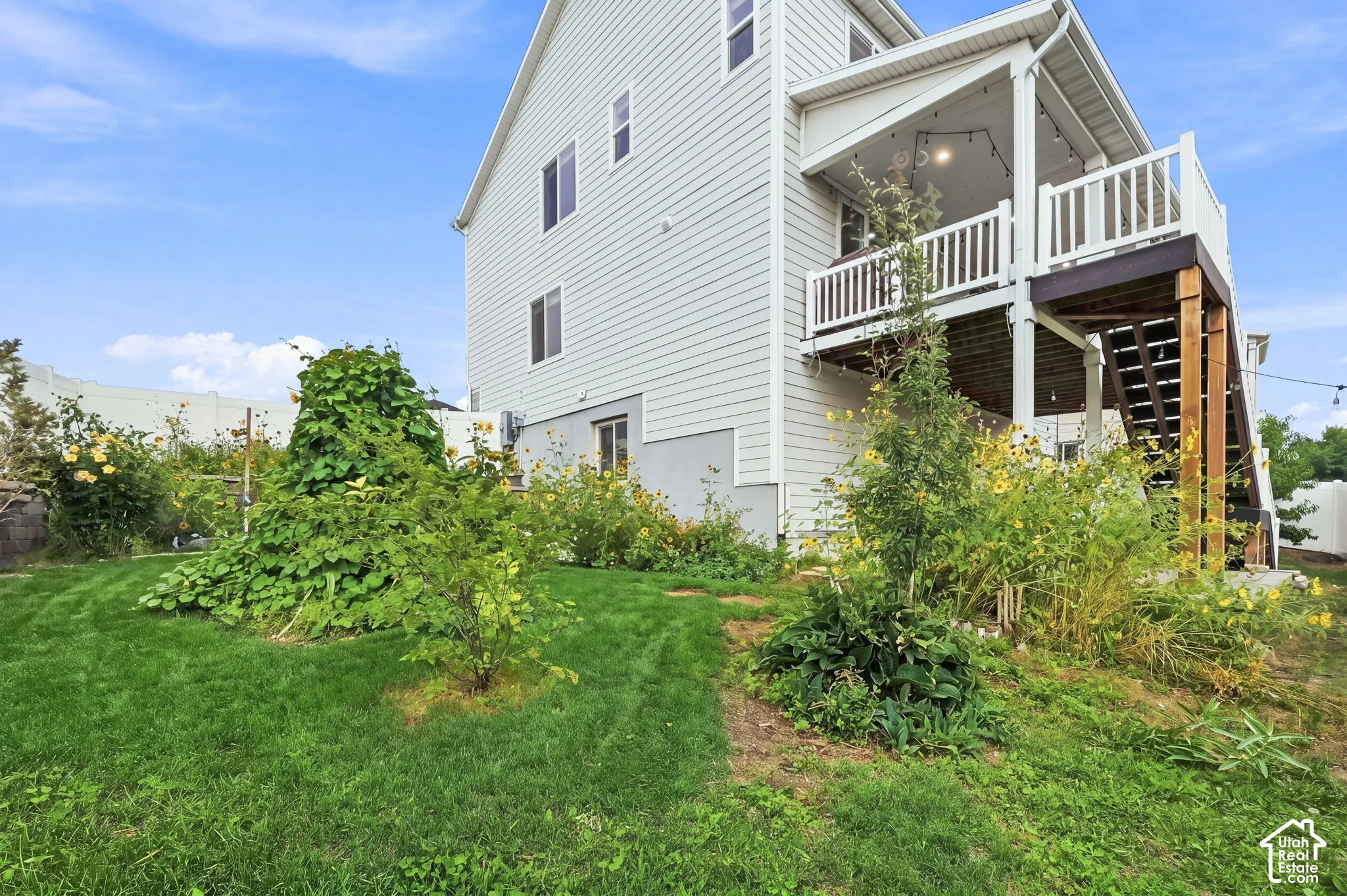 Two-story exterior featuring light-toned horizontal siding, a raised wooden deck with white railing, and a private backyard with established greenery