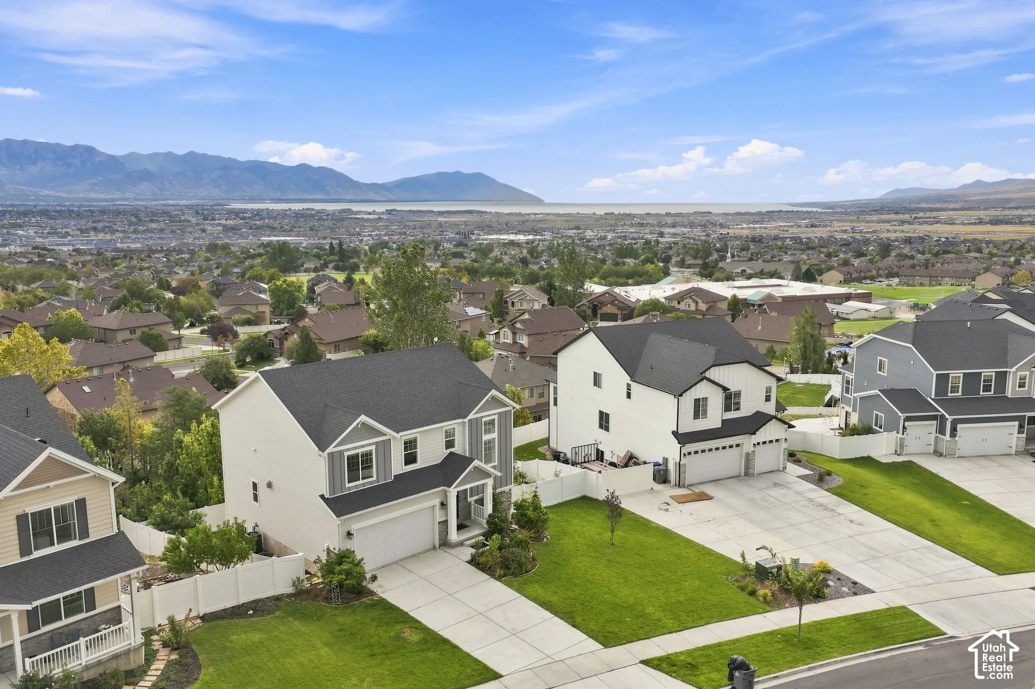Aerial perspective of the residential property featuring a white exterior, multi-pitched roofline, concrete driveway, attached garage, and white vinyl privacy fencing