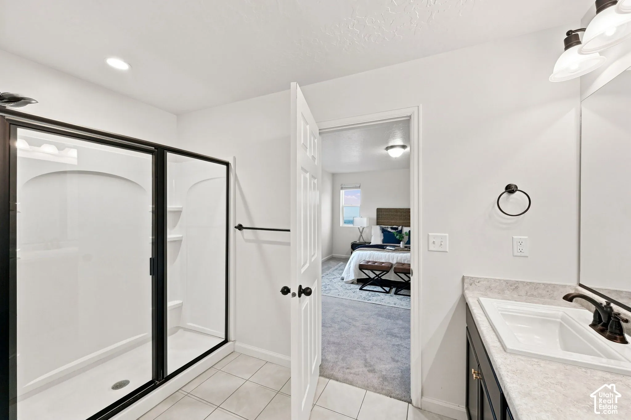 Bathroom featuring a walk-in shower with a black-framed glass enclosure, dark-toned cabinetry, light-toned stone-finish countertop, and wall-mounted vanity lighting