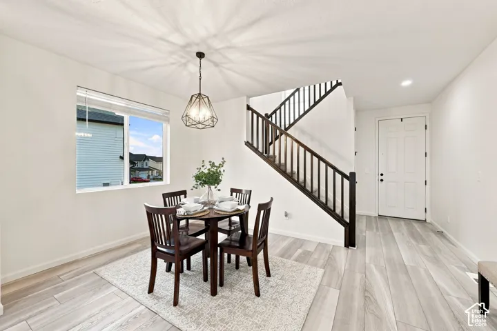 Open floor plan featuring wood-finish flooring, a geometric pendant light fixture, and a staircase with a dark wood-finish railing