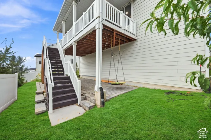 Multi-level exterior featuring a covered patio with paver flooring, elevated wood deck with white railings, and external staircase