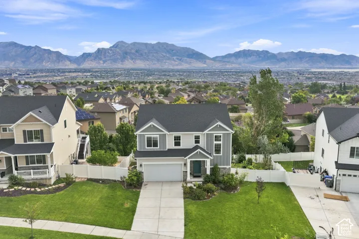 Two-story residence featuring a mixed-material exterior of horizontal lap siding and vertical board-and-batten, a front-facing attached garage, a concrete driveway, a white vinyl privacy fence, and an expansive mountain backdrop