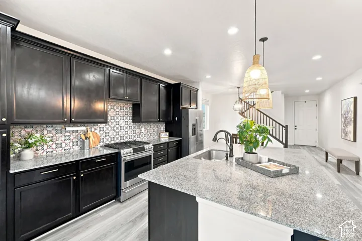 Kitchen featuring dark cabinetry, stone-surface countertops, decorative tile backsplash, stainless steel gas range, and a center island with an undermount sink