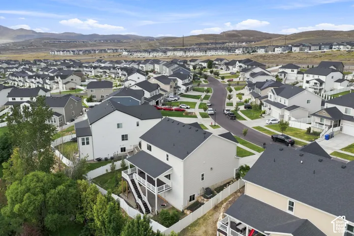 Aerial perspective featuring a two-story home with an elevated rear deck, a white vinyl perimeter fence, and mountain landscape backdrop