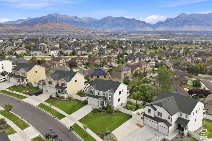 Aerial perspective of a suburban neighborhood featuring residential homes, paved streets, manicured lawns, white vinyl fencing, and a mountain range backdrop