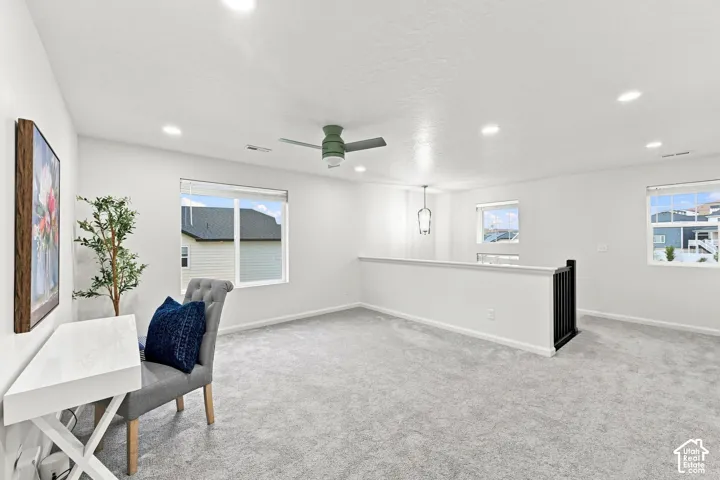 Open-concept interior featuring neutral carpeting, recessed lighting, a ceiling fan, and a staircase with a dark-finish railing