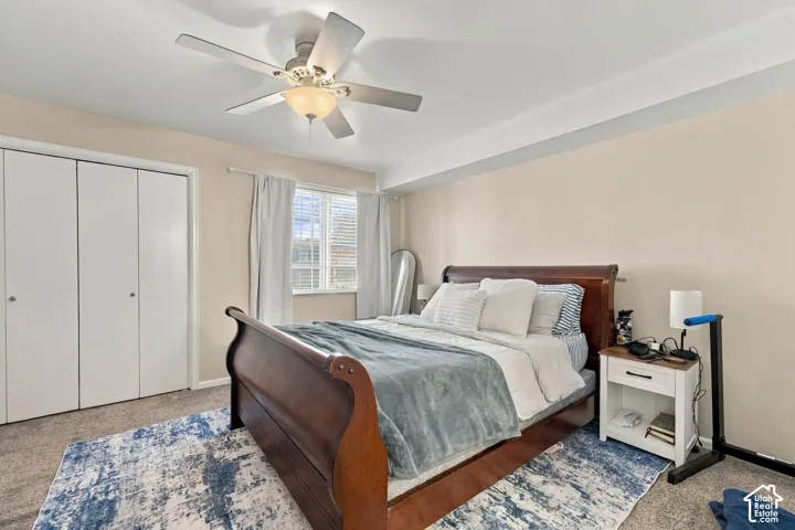 Bedroom featuring neutral wall paint, carpeted flooring, a ceiling fan with integrated light fixture, and floor-to-ceiling bi-fold closet doors