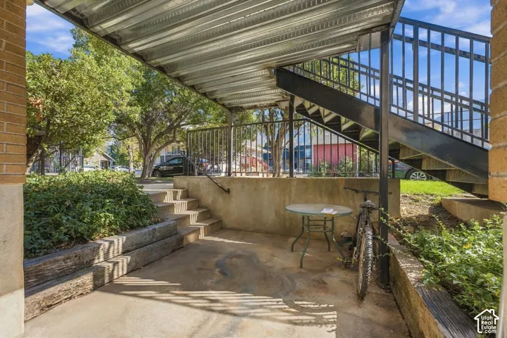 Covered concrete patio with overhead corrugated metal roofing, integrated metal staircase, and timber retaining walls