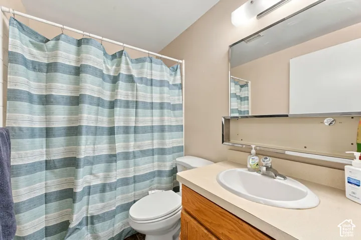 Wood-finish cabinetry featuring a light-toned countertop, integrated basin, chrome faucet, and large rectangular vanity mirror with built-in lighting