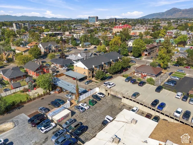 Aerial perspective of a multi-unit residential complex featuring a paved parking lot, covered parking structures, perimeter fencing, and mountain range backdrop