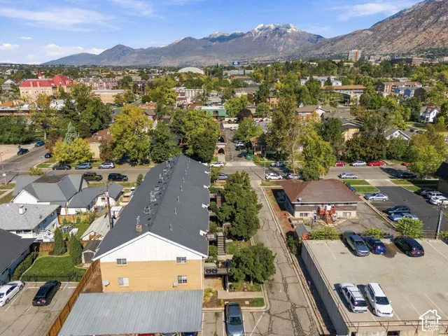 Aerial perspective featuring a multi-unit structure with a gabled roof, brick and vertical siding exterior, covered carport, and mountain range backdrop