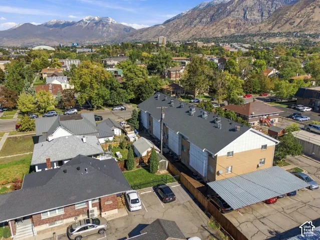 Aerial perspective featuring a multi-story brick and siding structure with a covered parking area, paved surface parking, and mountainous backdrop