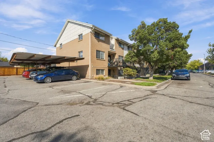 Multi-story building with brick and siding exterior, featuring a covered carport and paved surface parking