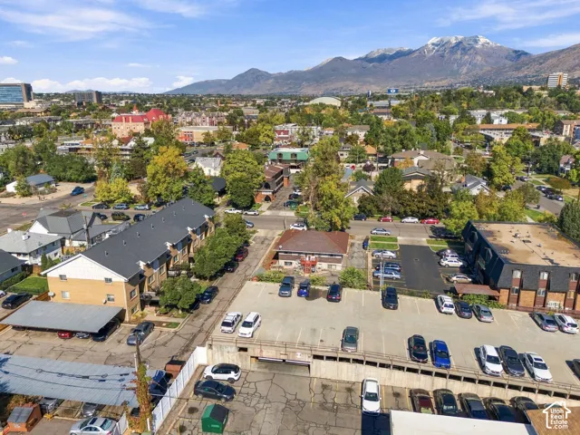 Aerial perspective featuring an extensive asphalt parking surface with designated spaces, covered parking structures, and a prominent mountain range backdrop