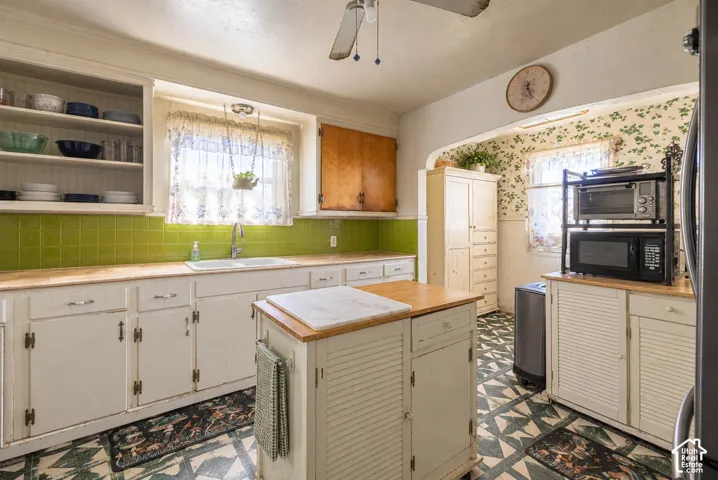 Kitchen featuring white cabinetry, green tile backsplash, open shelving, butcher-block style countertop, and built-in cabinetry  (Photo has been virtually decluttered)
