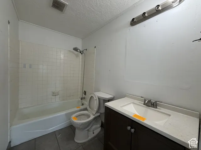 Bathroom featuring a vanity with a light-toned countertop, integrated basin, dark wood-finish cabinetry, tile flooring, and a shower-tub combination with tiled surround