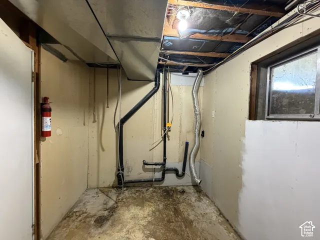 Utility area featuring exposed ceiling joists, concrete flooring, dedicated plumbing infrastructure, and a rectangular window