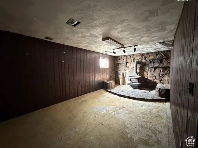 Stone fireplace feature with a raised stone hearth and wood-burning stove, paneled walls, and track lighting