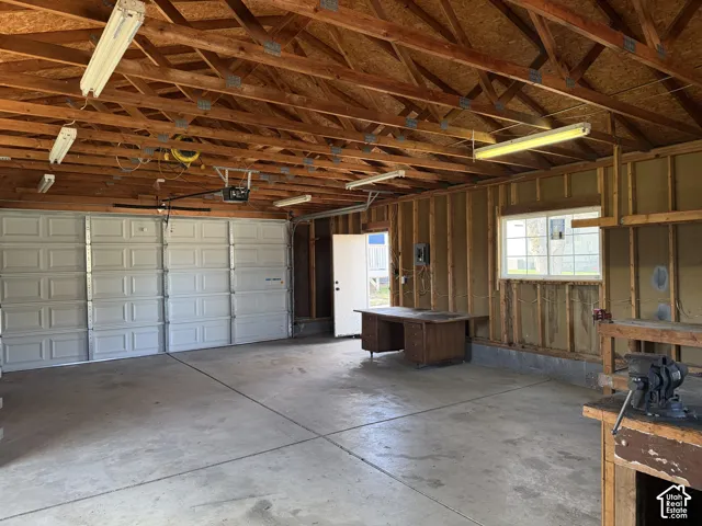 Multi-car garage featuring a concrete floor, exposed wood rafters, fluorescent lighting, and a window