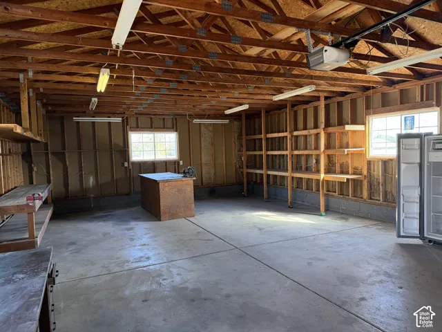 Garage space featuring exposed timber framing, concrete flooring, dual windows for natural light, wall-mounted wood shelving, and built-in workbench surfaces