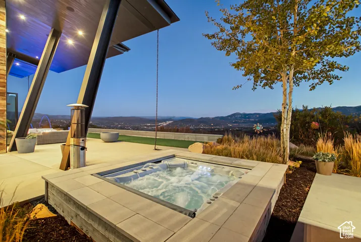 Covered outdoor patio with an integrated in-ground spa, stone paver surround, recessed ceiling lighting, and exposed steel structural supports
