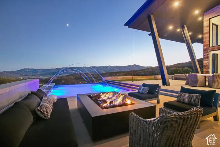 Outdoor patio featuring an integrated fire pit, infinity-edge swimming pool with water features, covered terrace, and mountain backdrop