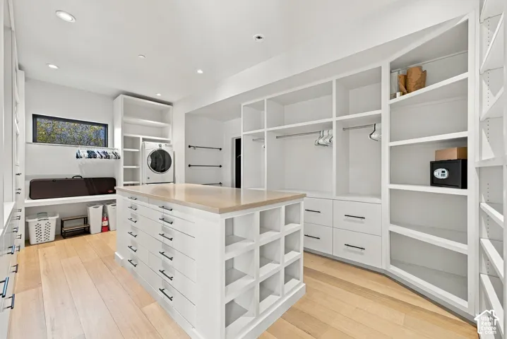 Custom walk-in closet in Primary Suite, featuring floor-to-ceiling built-in shelving, a central island with storage drawers and quartz countertop, wood-finish flooring, and integrated laundry