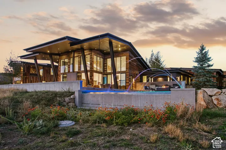 Contemporary residence featuring a wood-clad exterior, expansive floor-to-ceiling windows, dramatic angled rooflines, an infinity-edge pool, and integrated concrete retaining walls