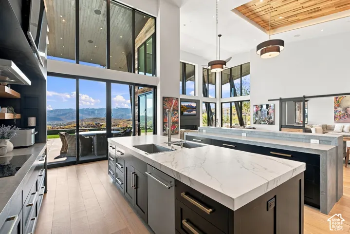Expansive interior featuring floor-to-ceiling windows, wood-finish flooring, a kitchen island with stone countertops, a coffered wood-paneled ceiling, and sliding glass doors