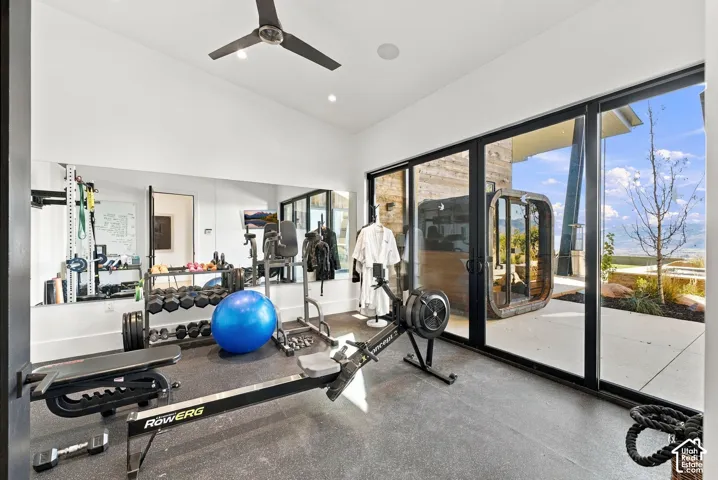 Gym with vaulted ceilings wall-to-wall mirrors, large glass sliding doors opening to an exterior concrete patio with inspiring views and direct sauna access.