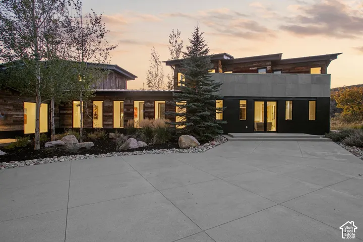 Modern architectural exterior featuring wood-plank siding, large-format paneling, shed rooflines, an expansive concrete driveway, and custom hardscaping