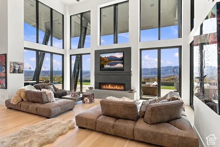 Double-height ceilings with floor-to-ceiling windows, linear fireplace with custom surround, wood-finish flooring, and pass through views toward Park City