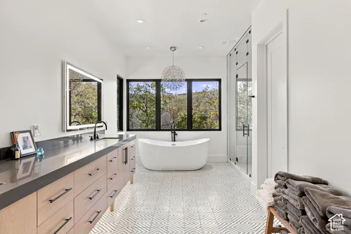 Primary bathroom featuring dual lighted vanities, freestanding soaking tub, glass-enclosed steam shower with full-height stone-finish wall tile, patterned geometric floor tile, and oversized windows to capture mountain views