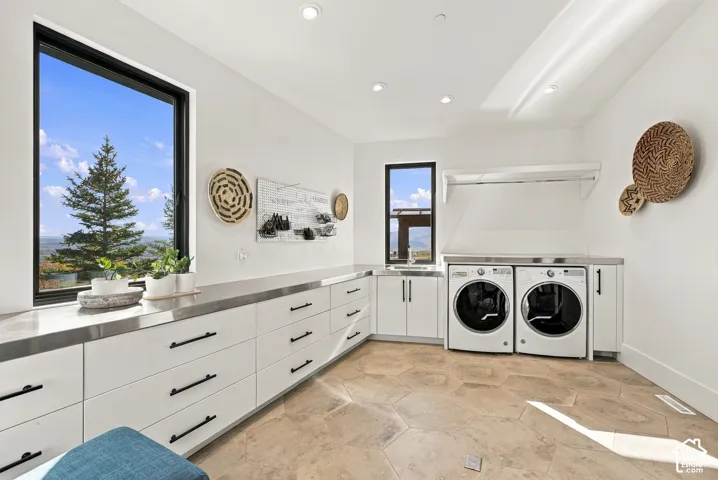 Laundry room featuring large-format hexagonal floor tile, extensive white cabinetry with matte black hardware, metallic countertops, integrated sink, and recessed lighting