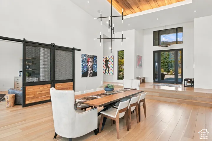 High ceilings featuring a wood-plank inset, structural metal-framed sliding partition doors, wide-plank wood-finish flooring, modern multi-arm chandelier, and a glass-paneled entry door