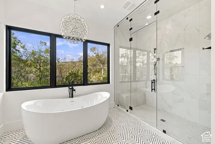 Primary bathroom featuring freestanding soaking tub, glass-enclosed steam shower with full-height stone-finish wall tile, patterned geometric floor tile, and oversized windows to capture mountain views