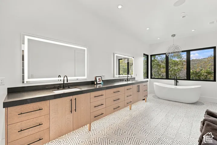 Primary bathroom featuring dual lighted vanities, freestanding soaking tub, glass-enclosed steam shower with full-height stone-finish wall tile, patterned geometric floor tile, and oversized windows to capture mountain views