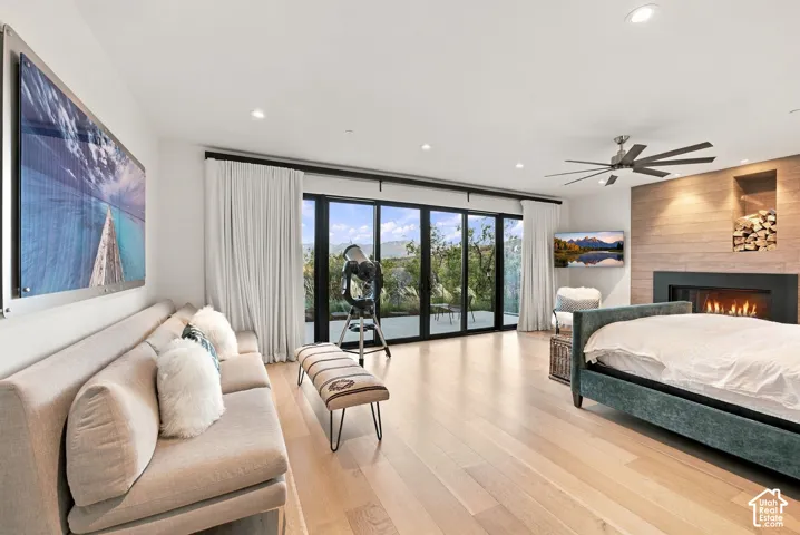 Primary bedroom featuring views toward Park City, wide-plank wood-finish flooring, floor-to-ceiling sliding glass doors, horizontal wood-paneled accent wall, built-in gas fireplace