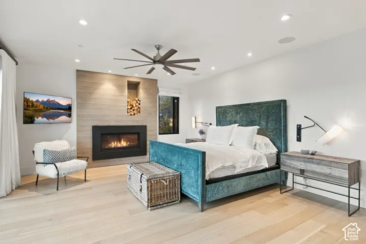 Primary bedroom featuring views toward Park City, wide-plank wood-finish flooring, floor-to-ceiling sliding glass doors, horizontal wood-paneled accent wall, built-in gas fireplace